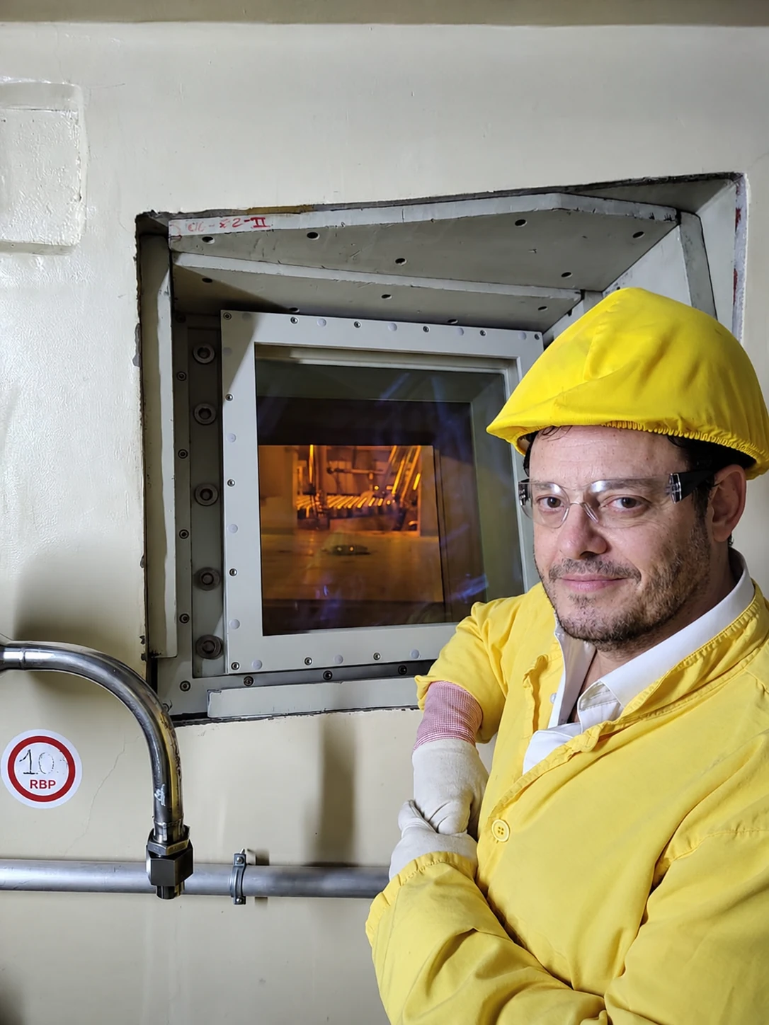 Demian Reidel en Atucha II, mirando por la ventana de observación del reactor con indumentaria protectora amarilla